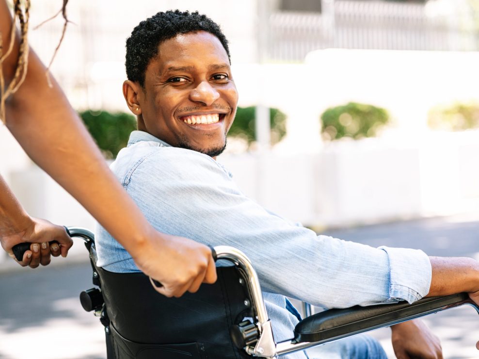 Man in a wheelchair smiling and looking at camera. An African American man in a wheelchair smiling and looking at the camera while his girlfriend pushing him.
